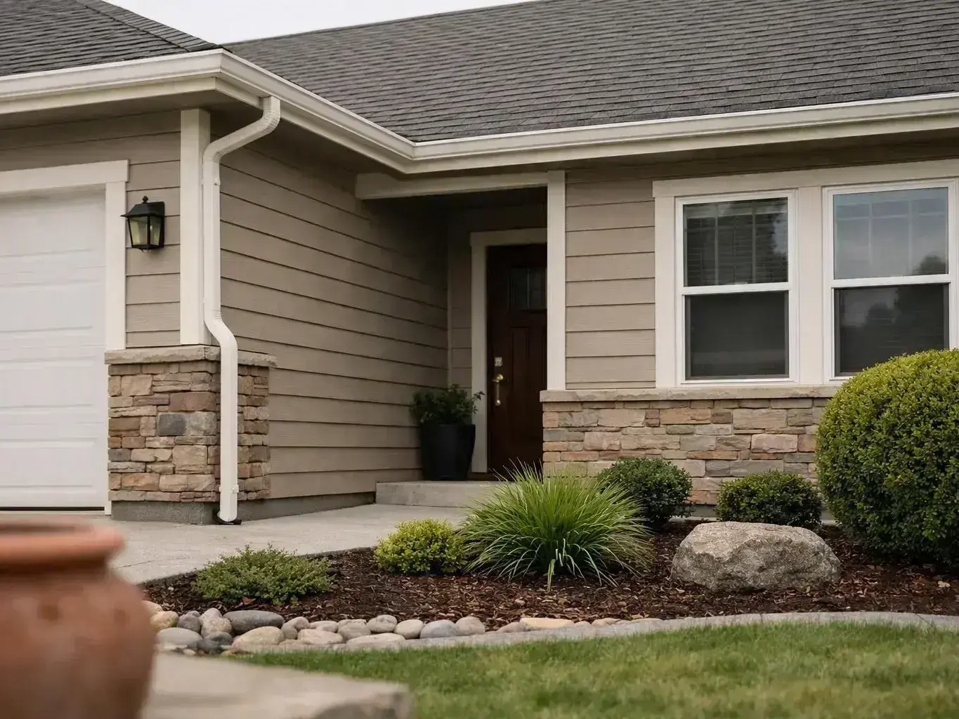 A beige house exterior shows a garage, front door, windows, and a landscaped front yard