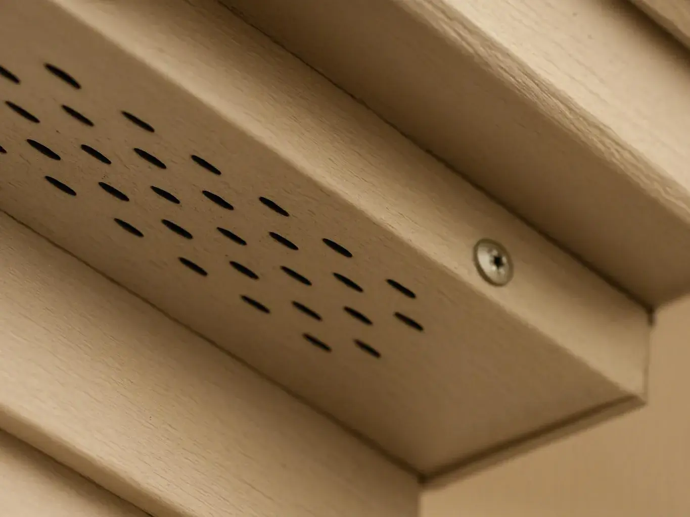 Close-up of a beige metal vent panel with rows of black slits and a screw in the corner
