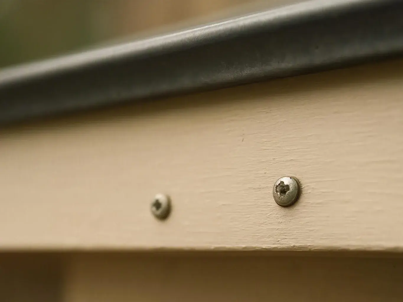 Close-up of a beige wooden board with two screws and a dark metal strip along the top