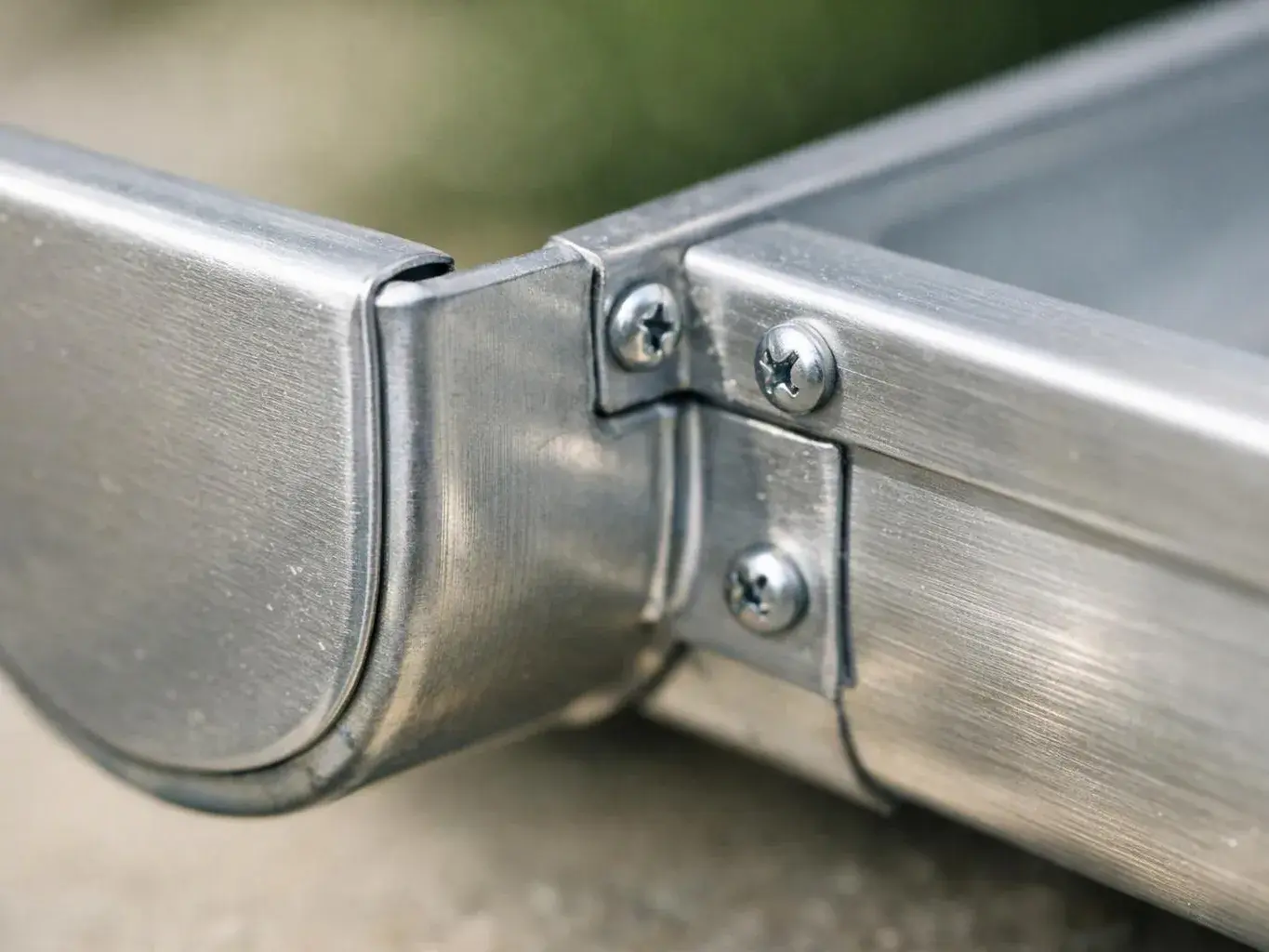 Close-up of a brushed metal gutter joint with screws and a curved end cap