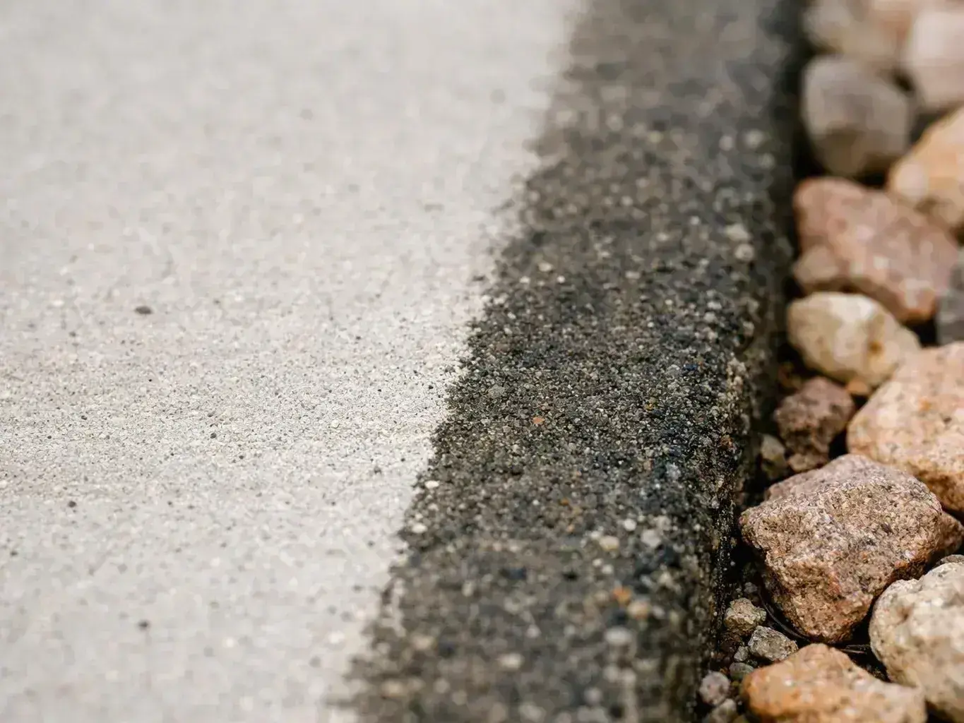 Close-up of a concrete edge beside dark asphalt and scattered rocks