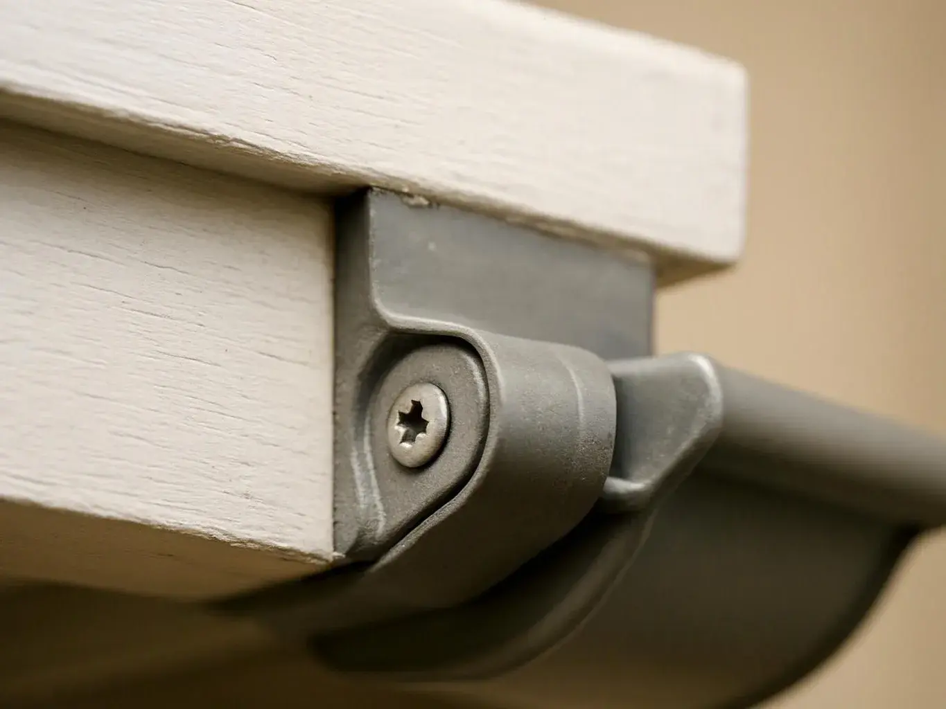Close-up of a gray metal bracket and screw attached to a white wooden surface against a beige background