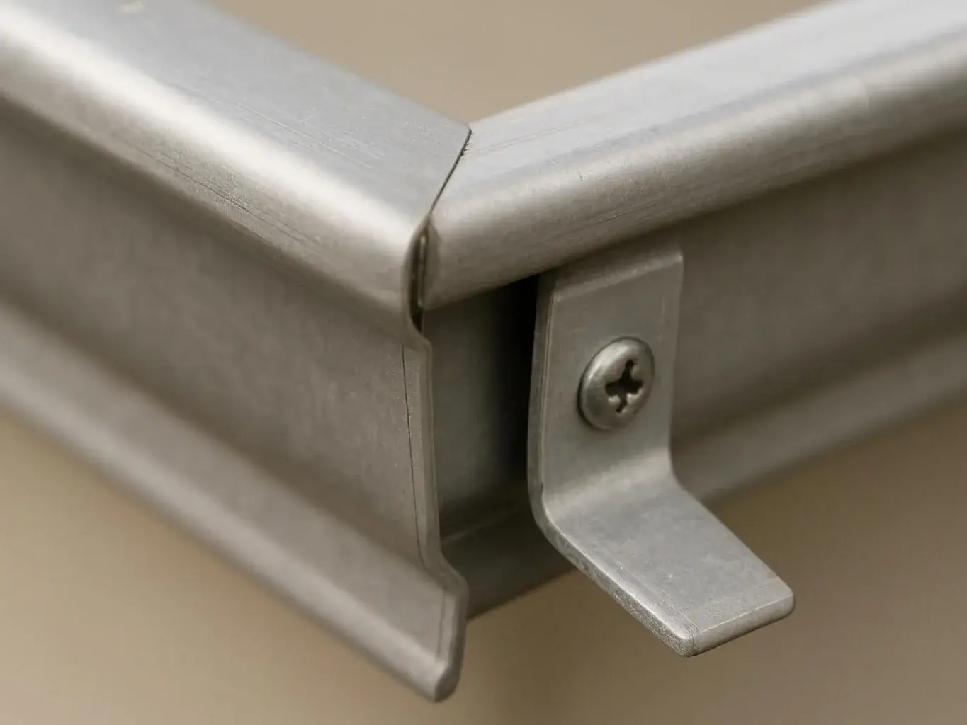 Close-up of a metal corner joint with a small screw and bracket against a plain beige background