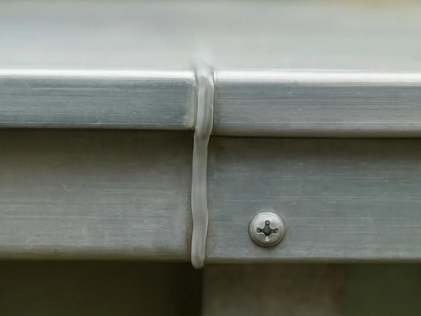 Close-up of a metal gutter joint sealed with a strip and a visible screw against a wall