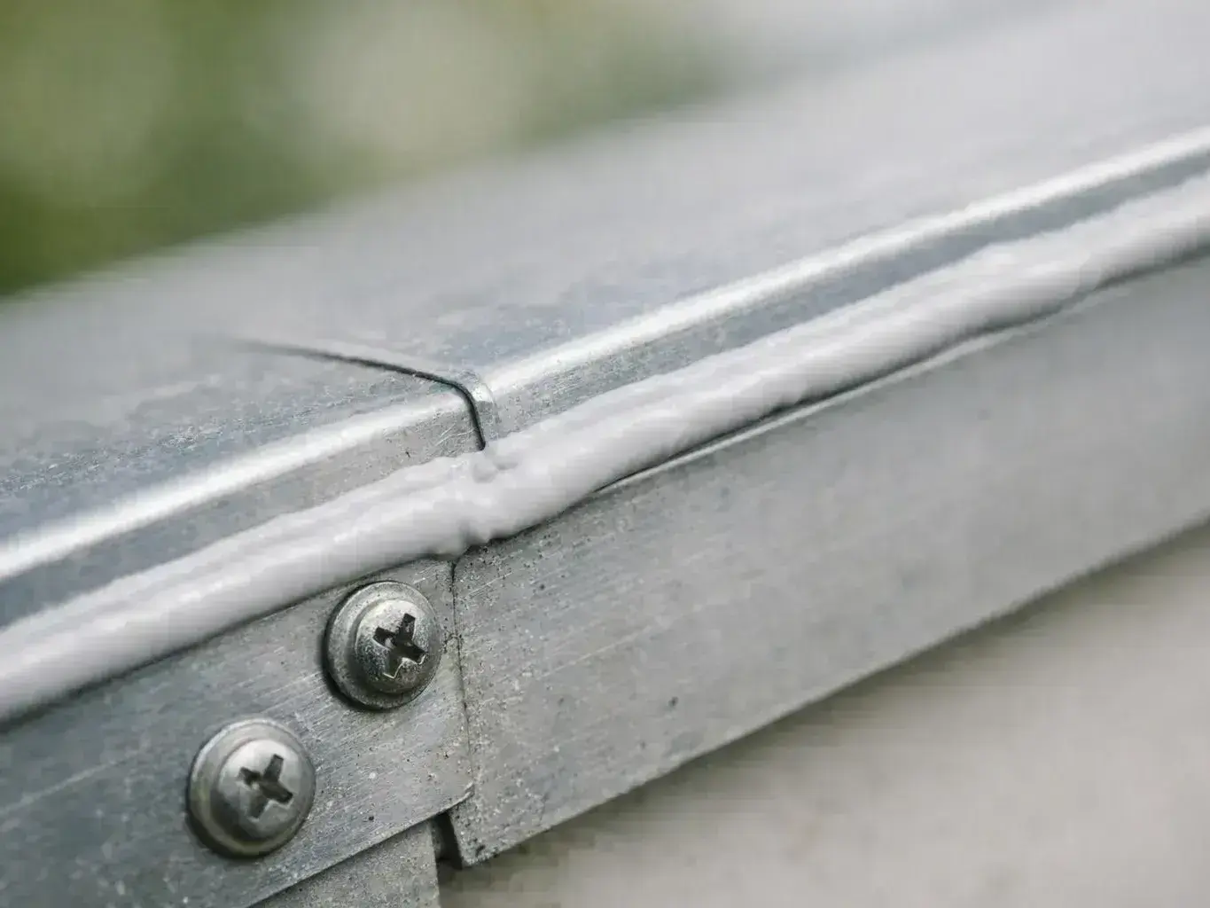 Close-up of a metal seam with screws and a bead of white sealant along the joint