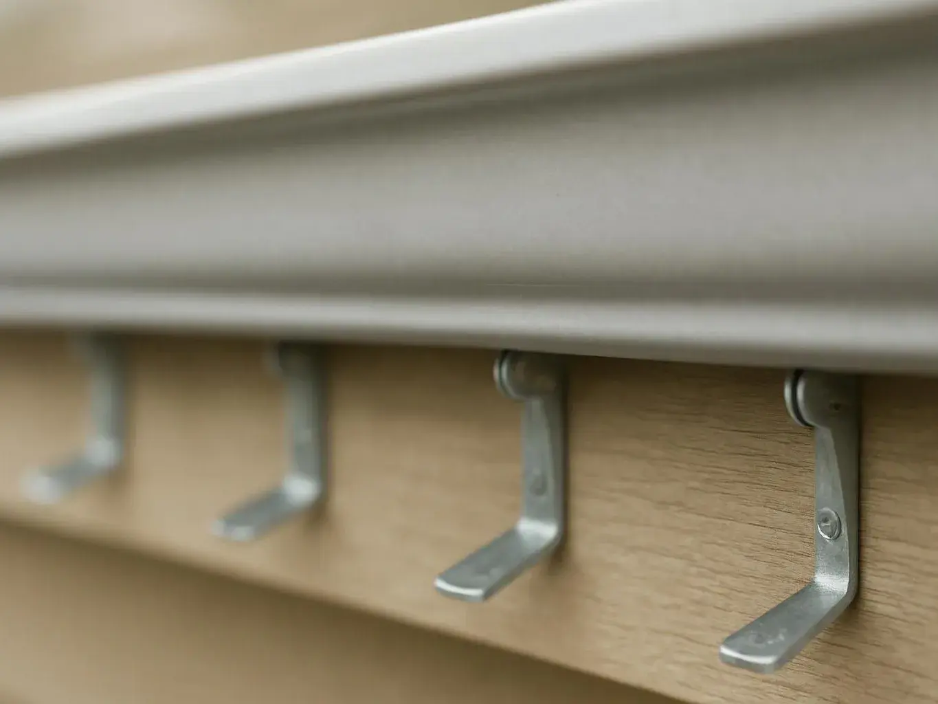 Close-up of metal wall hooks mounted on a wooden board beneath a white ledge
