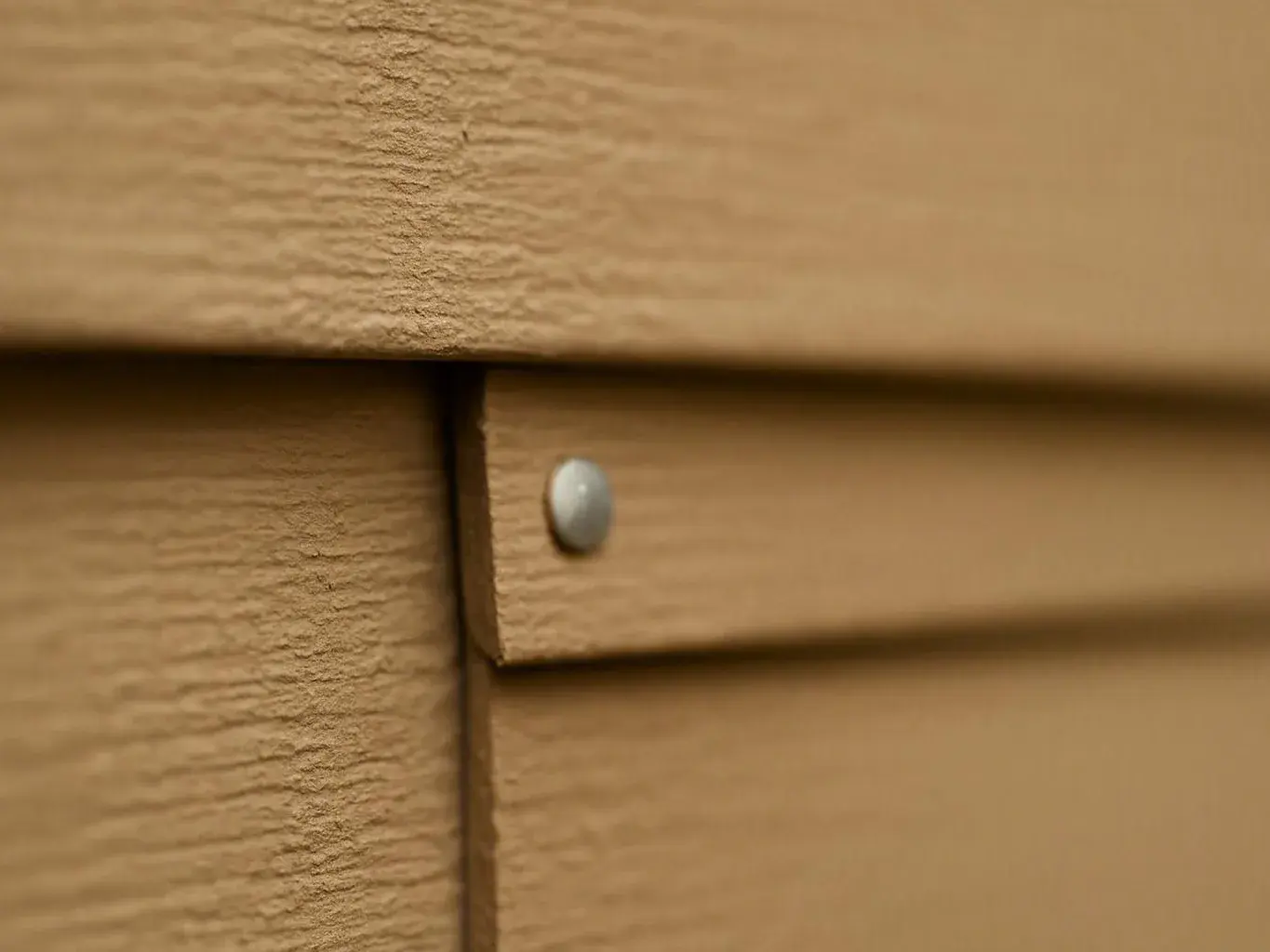 Close-up of tan wooden siding with a small silver nail and a narrow seam