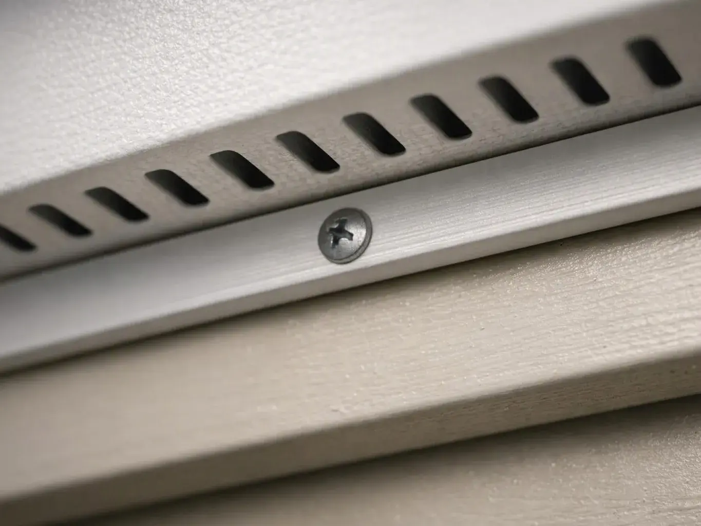 Close-up of a vented metal panel with a single screw on a textured surface