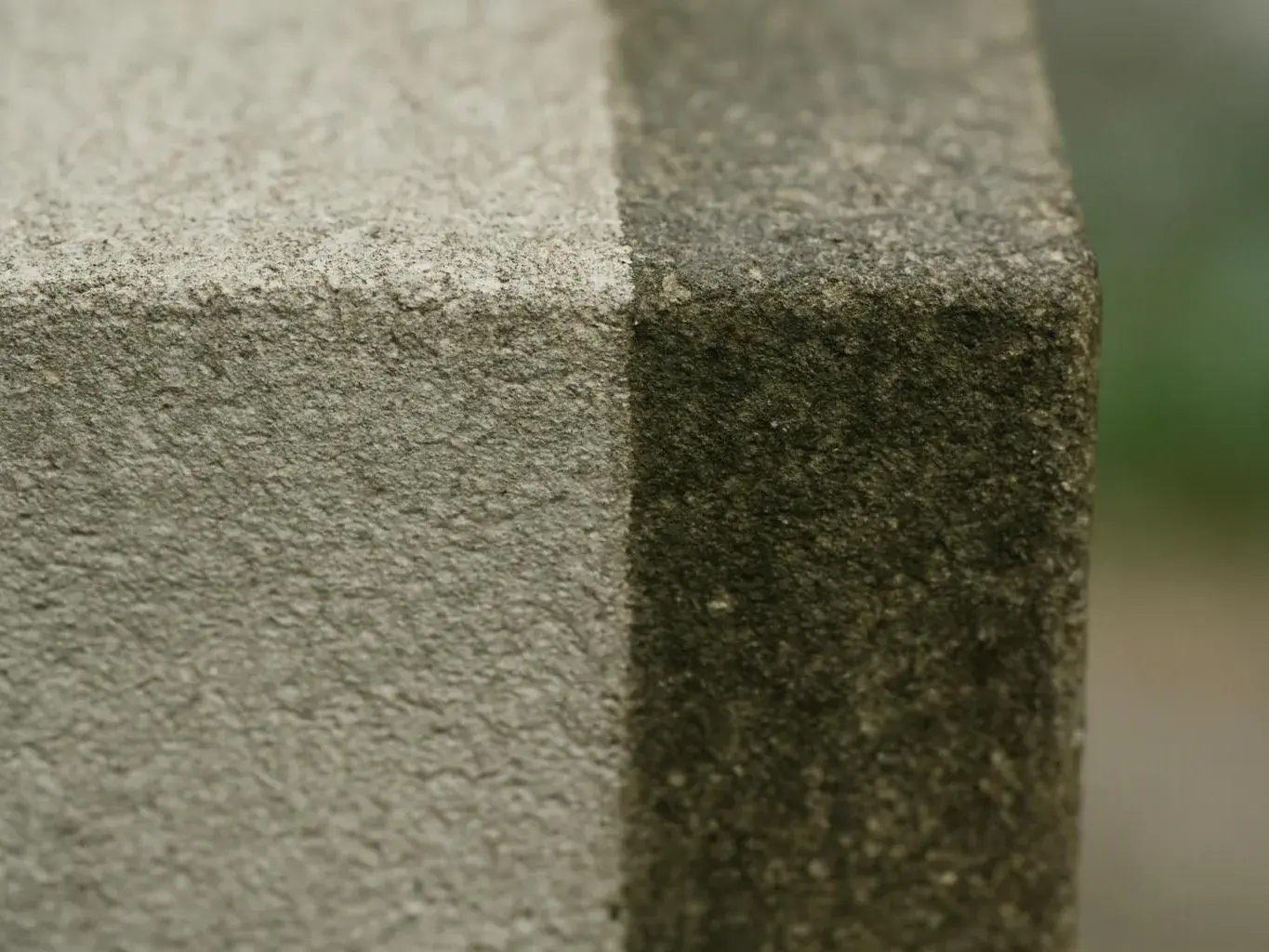 Close-up of a weathered stone corner with rough texture and dark moss growth