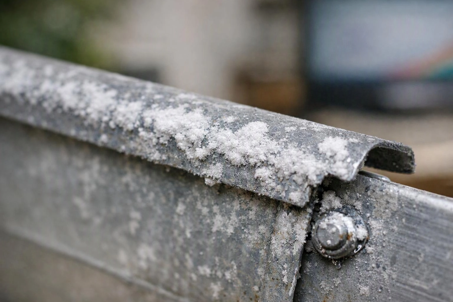 A frost-covered metal rail with a visible bolt stretches across a blurred outdoor background