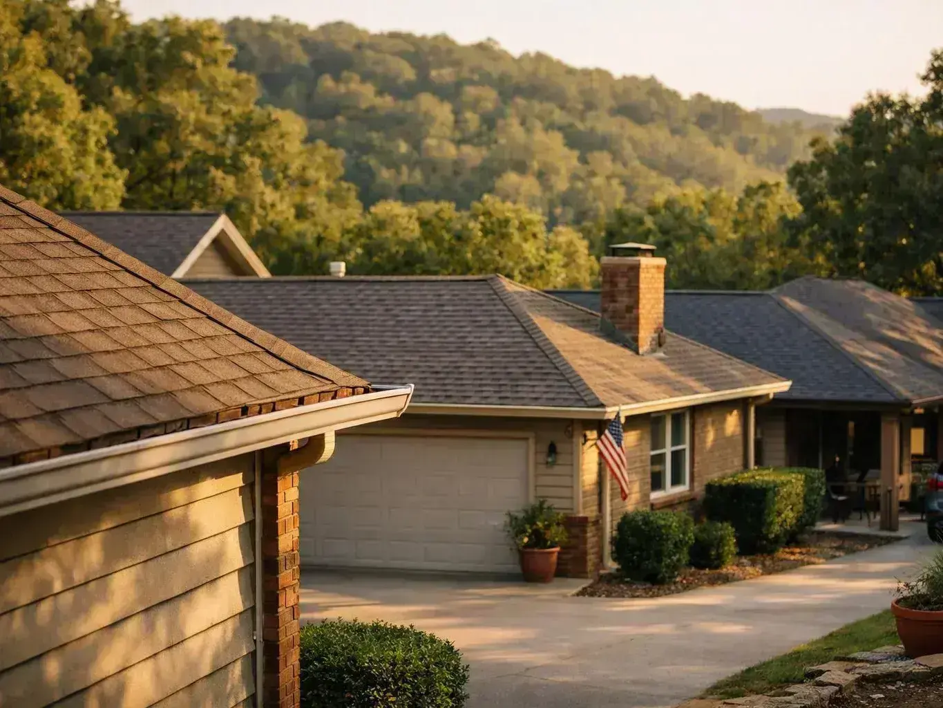 Suburban houses line a sloping driveway with trees and hills in warm evening light