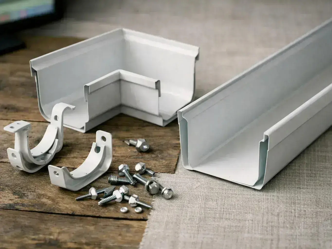 White metal gutter parts, brackets, and screws lie spread across a wooden table